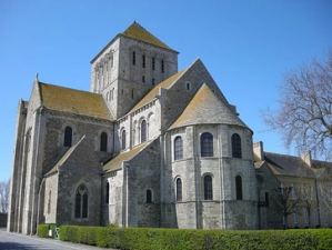 a large stone building with a clock tower in front of a house with Pluscarden Abbey in the background