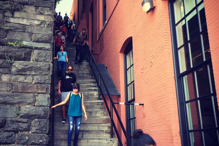 a group of people walking down a sidewalk in front of a brick building