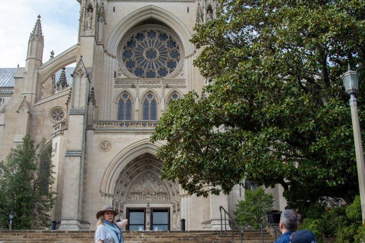 Tour guide pointing at large cathedral facade with group of people on steps.