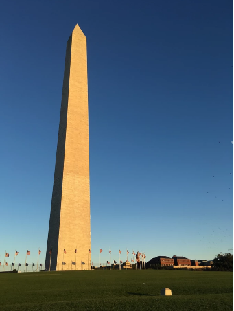 a large clock tower in the middle of a field with Washington Monument in the background