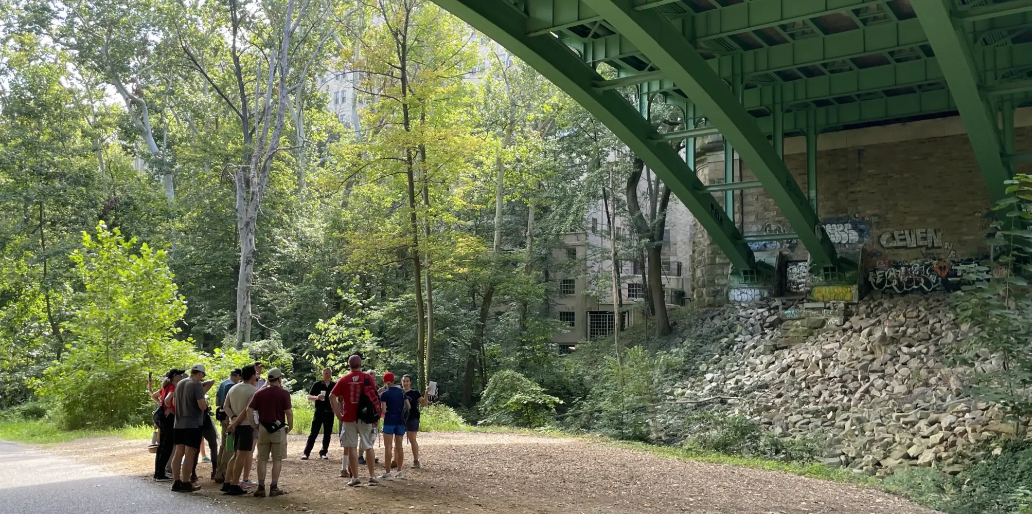 Group of people standing under a green bridge in a wooded area.